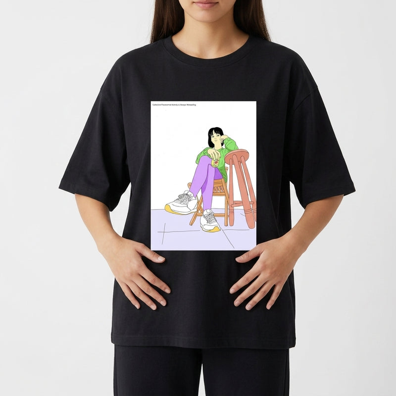 Camiseta com estampa frontal de uma figura feminina sentada de forma relaxada em uma cadeira, usando roupas casuais e tênis, sobre superfície quadrada.