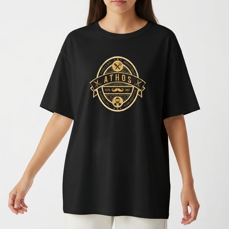 Camiseta com estampa frontal de emblema oval contendo texto "ATHOS", ferramentas, bigode, tesouras e barba, com detalhes e ornamentos circulares.