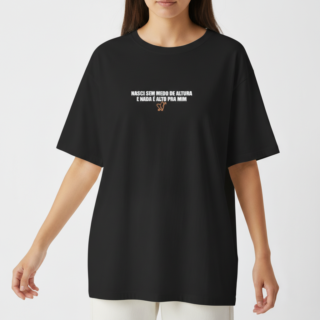 Camiseta com estampa frontal de texto "Nasci sem medo de altura e nada é alto pra mim" com detalhes gráficos e estampa traseira de mãos tatuadas com anéis.