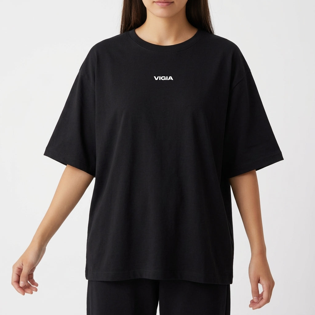 Camiseta com estampa frontal de logo pequeno escrito “VIGIA” no centro e estampa traseira de controle de videogame com frase “DEUS ESTÁ NO CONTROLE”.