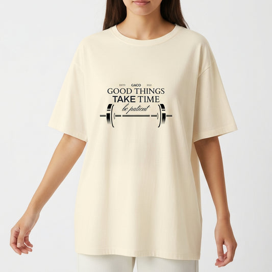 Camiseta com estampa frontal de uma barra de peso acompanhada da frase "GOOD THINGS TAKE TIME, be patient", decorando o centro com estilo motivacional.