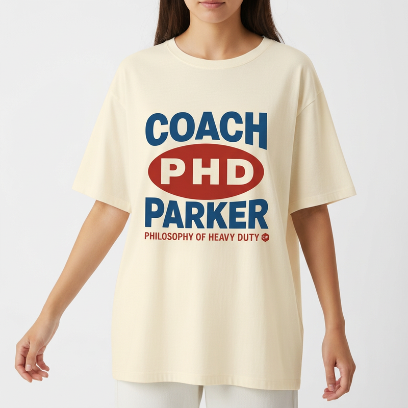 Camiseta com estampa frontal de texto em destaque centralizado, incluindo letras maiúsculas "COACH PHD PARKER" e frase complementar na parte inferior.