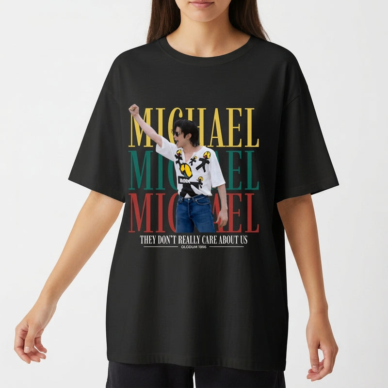Camiseta com estampa frontal de um artista performando, sobreposta a três repetições do nome "Michael" em amarelo, verde e vermelho, acompanhada da frase "They Don't Really Care About Us".