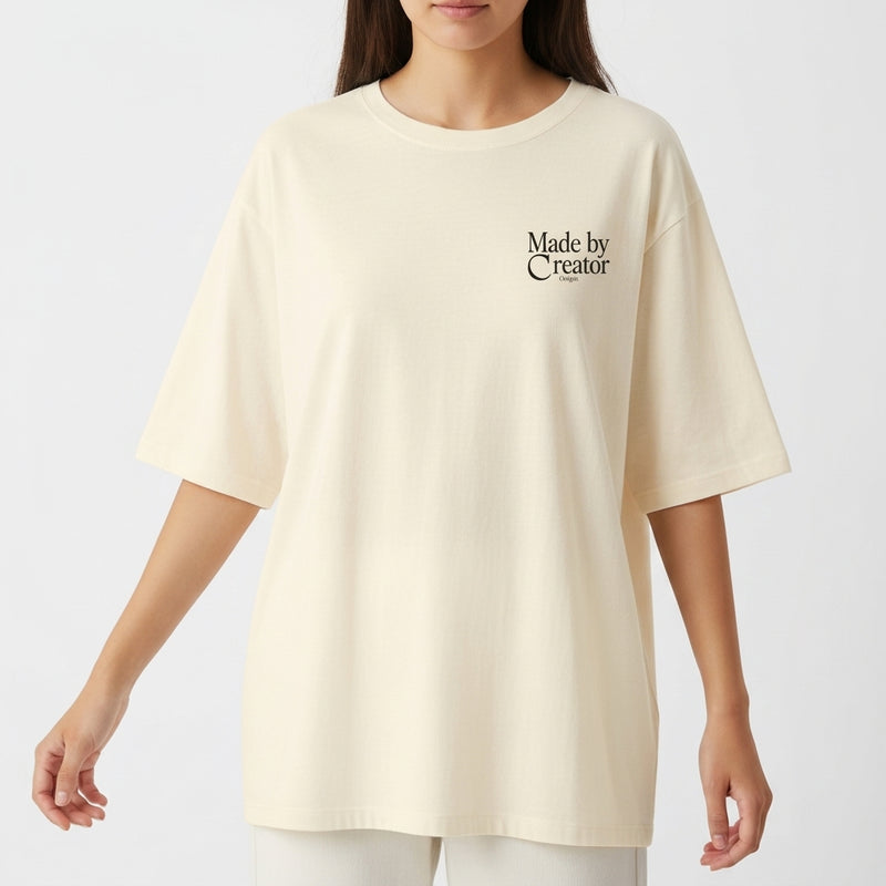 Camiseta com estampa frontal de "Made by Creator" em letras estilizadas e estampa traseira de "Made by Creator" acompanhada por ilustração de flores coloridas.