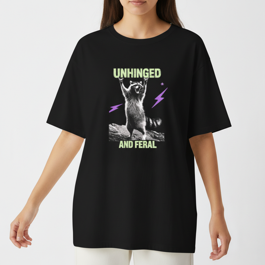 Camiseta com estampa frontal de guaxinim em pose exuberante entre raios estilizados, acompanhada das palavras "Unhinged" e "And Feral" em fonte marcante.