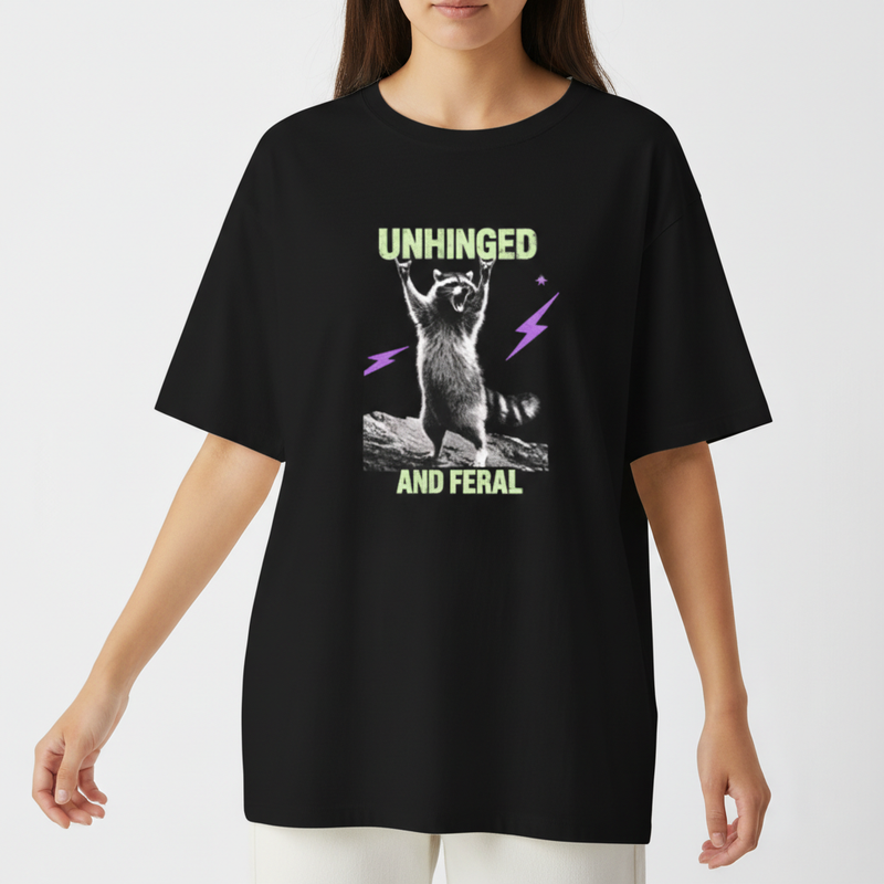 Camiseta com estampa frontal de guaxinim em pose exuberante entre raios estilizados, acompanhada das palavras "Unhinged" e "And Feral" em fonte marcante.