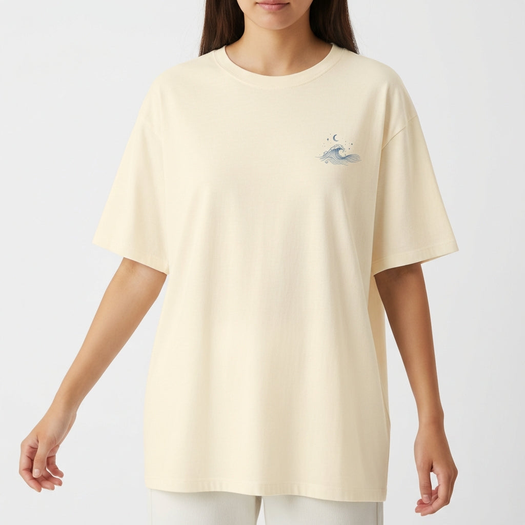 Camiseta com estampa frontal de uma pequena onda estilizada, acompanhada por elementos celestiais como estrelas e uma lua crescente acima dela.
