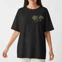 Camiseta com estampa frontal de design intrincado com elementos florais ao redor de texto e estampa traseira de figura mística centralizada com ornamentos detalhados.