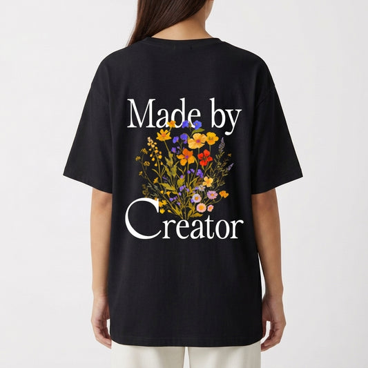 Camiseta com estampa frontal de texto estilizado "Made by Creator" e estampa traseira de flores vibrantes entre o texto "Made by Creator".