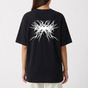 Camiseta com estampa frontal de texto estilizado "Pântano 3000" em um design de respingos e estampa traseira com padrão abstracto intrincado com elementos pontiagudos.