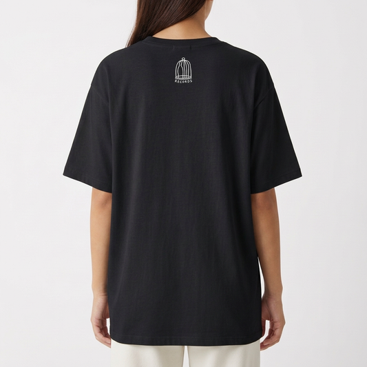 Camiseta com estampa frontal de figuras alienígenas e humanoides interagindo, acompanhadas de um texto estilizado; e estampa traseira de uma gaiola minimalista.