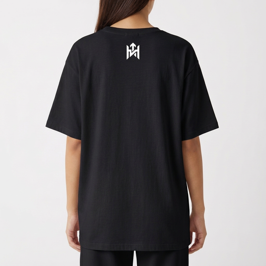Camiseta com estampa frontal de rosto sorridente decorado com folhas e texto "Elevate Your Frequency" emoldurado por elementos naturais e estampa traseira de símbolo geométrico simples próximo à gola.