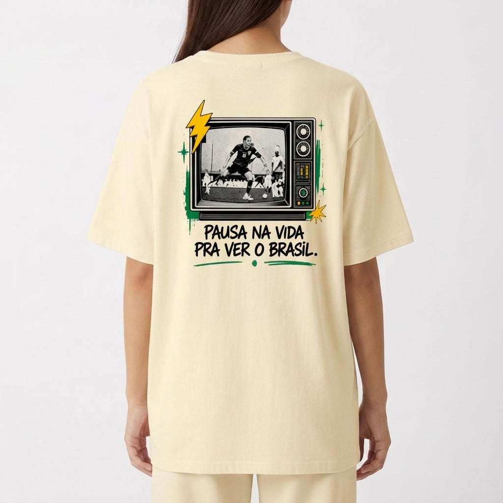 Camiseta com estampa frontal de "Modo Brasil On" ao lado de um raio estilizado e estampa traseira de TV retrô com jogador de futebol e frase inspiradora.