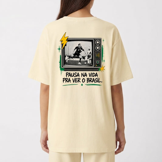Camiseta com estampa frontal de "Modo Brasil On" ao lado de um raio estilizado e estampa traseira de TV retrô com jogador de futebol e frase inspiradora.