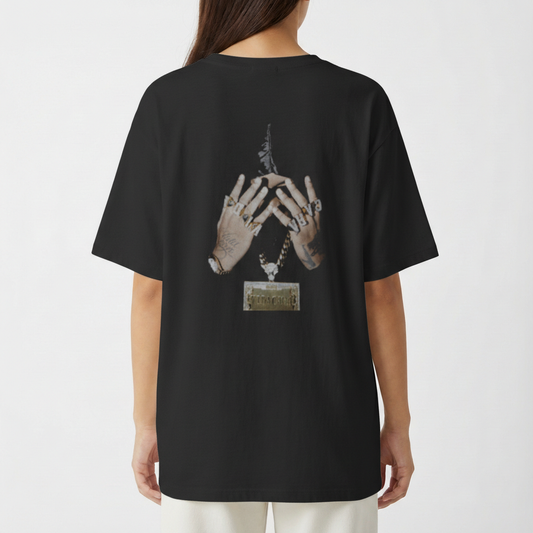 Camiseta com estampa frontal de texto "Nasci sem medo de altura e nada é alto pra mim" com detalhes gráficos e estampa traseira de mãos tatuadas com anéis.