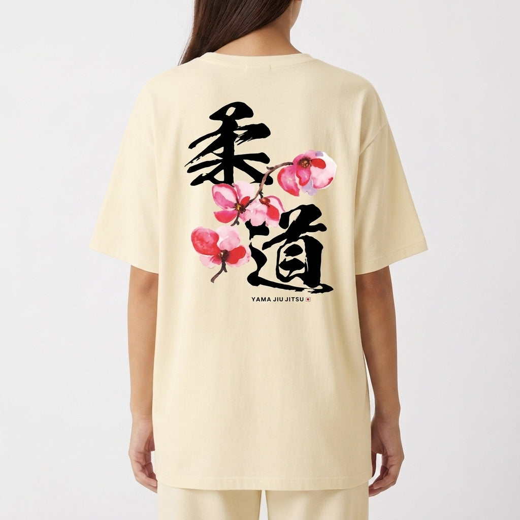 Camiseta com estampa frontal de texto "YAMA JIU JITSU" em letras pequenas e estampa traseira de caracteres japoneses grandes com flores estilizadas.