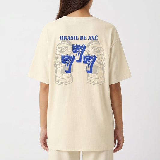 Camiseta com estampa frontal de brasão estilizado e estampa traseira de rosto tribal com "Brasil de Axé" acima e o número "777" em destaque.