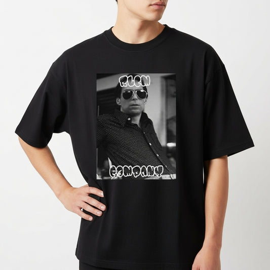 Camiseta com estampa frontal de fotografia em preto e branco de uma pessoa usando óculos escuros, com texto estilizado acima e abaixo da imagem.