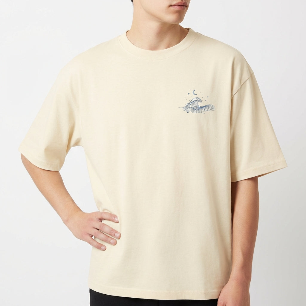 Camiseta com estampa frontal de uma pequena onda estilizada, acompanhada por elementos celestiais como estrelas e uma lua crescente acima dela.