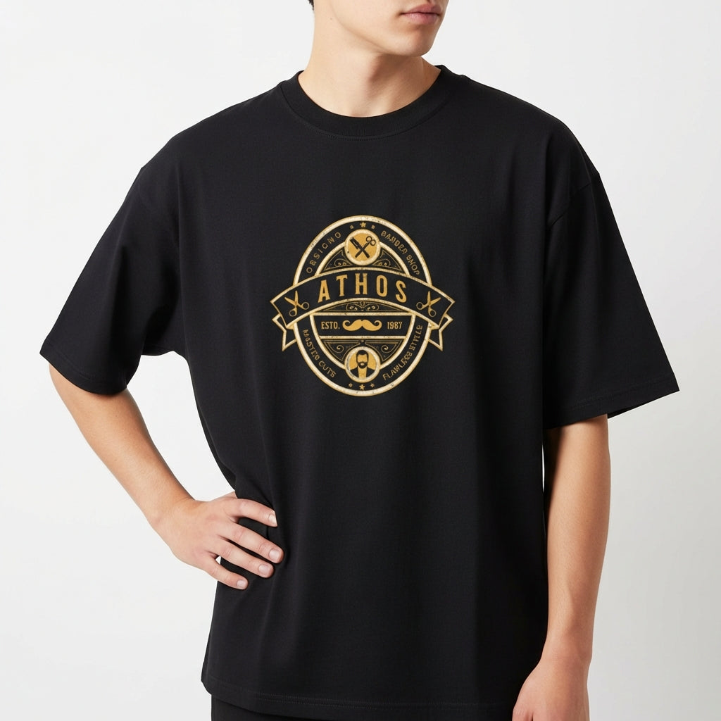 Camiseta com estampa frontal de emblema oval contendo texto "ATHOS", ferramentas, bigode, tesouras e barba, com detalhes e ornamentos circulares.