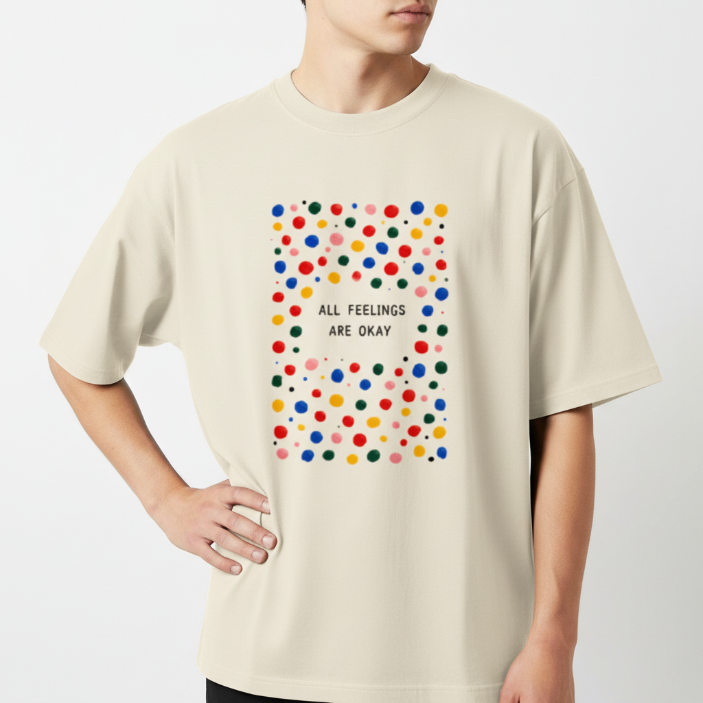 Camiseta com estampa frontal de padrão de bolinhas coloridas ao redor da frase central "ALL FEELINGS ARE OKAY", criando um visual vibrante e acolhedor.