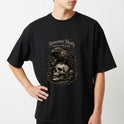 Camiseta com estampa frontal de caveira detalhada sobre flores com corvo pousado e texto estilizado na parte superior.