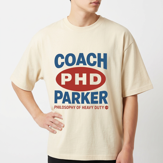 Camiseta com estampa frontal de texto em destaque centralizado, incluindo letras maiúsculas "COACH PHD PARKER" e frase complementar na parte inferior.
