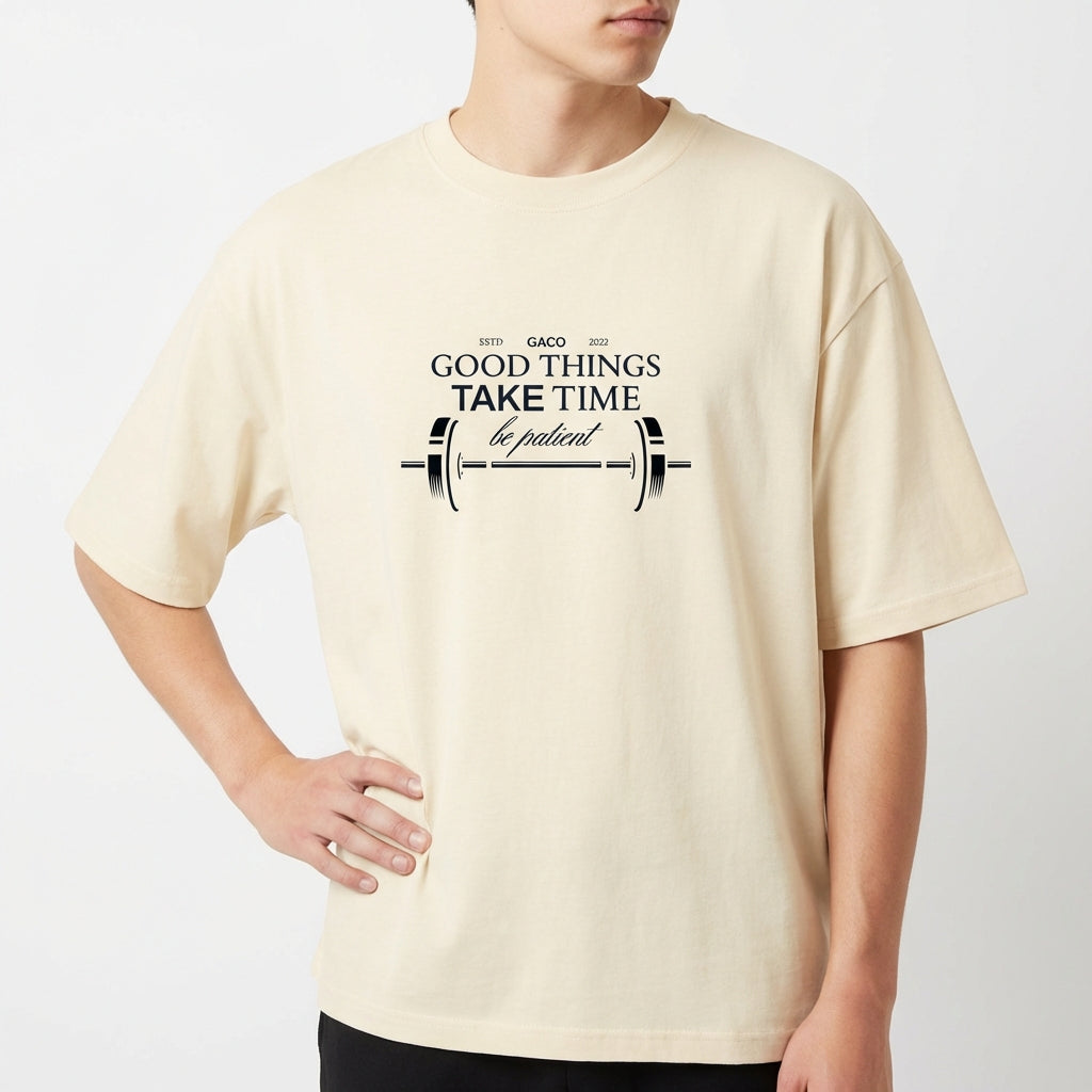 Camiseta com estampa frontal de uma barra de peso acompanhada da frase "GOOD THINGS TAKE TIME, be patient", decorando o centro com estilo motivacional.