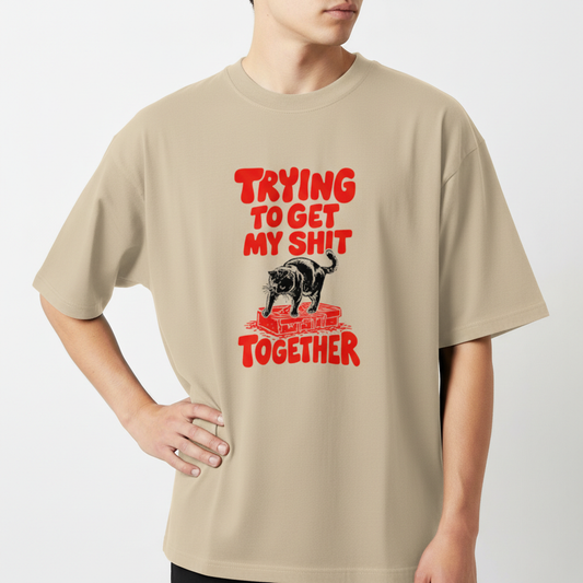 Camiseta com estampa frontal de um urso sobre blocos de construção com a frase em destaque "Trying to Get My Shit Together" em letras estilizadas.