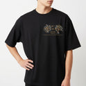 Camiseta com estampa frontal de design intrincado com elementos florais ao redor de texto e estampa traseira de figura mística centralizada com ornamentos detalhados.
