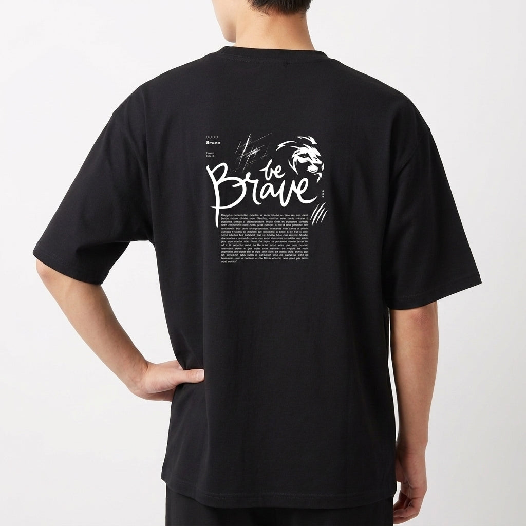 Camiseta com estampa frontal da palavra "brave" em letras estilizadas e efeito de brilho, e estampa traseira de texto "be brave" com desenho de leão.