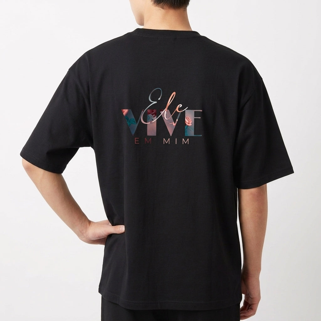 Camiseta com estampa frontal de "Verbo" estilizado centralizado e estampa traseira de frase artística "Ele Vive em Mim" com design tipográfico elegante.