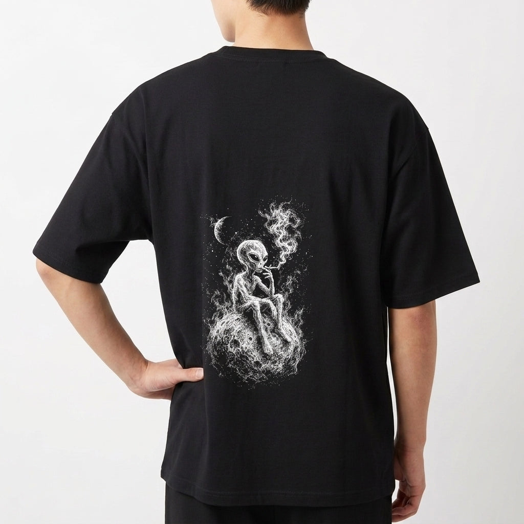 Camiseta com estampa traseira de alienígena sentado numa superfície rochosa, fumando com tranquilidade, envolto em uma atmosfera etérea e nebulosa sob a lua.