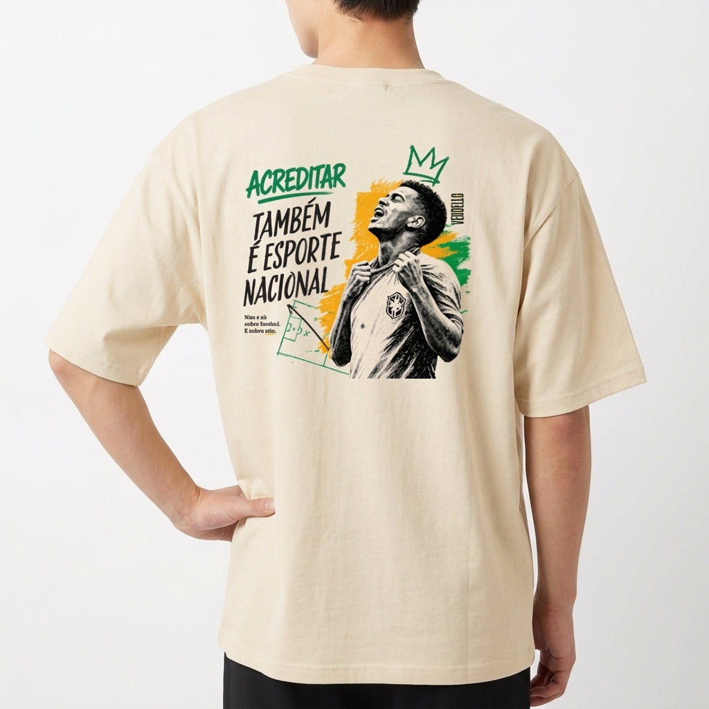 Camiseta com estampa frontal de pequena coroa e "ACREDITAR" estilizado, e estampa traseira de jogador com coroa, cores vibrantes e mensagem inspiradora.