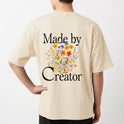 Camiseta com estampa frontal de "Made by Creator" em letras estilizadas e estampa traseira de "Made by Creator" acompanhada por ilustração de flores coloridas.