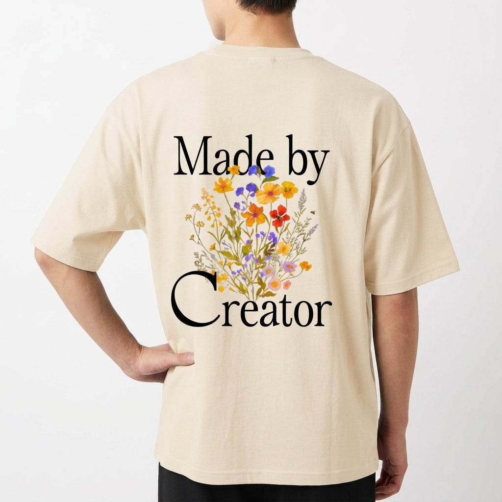 Camiseta com estampa frontal de "Made by Creator" em letras estilizadas e estampa traseira de "Made by Creator" acompanhada por ilustração de flores coloridas.