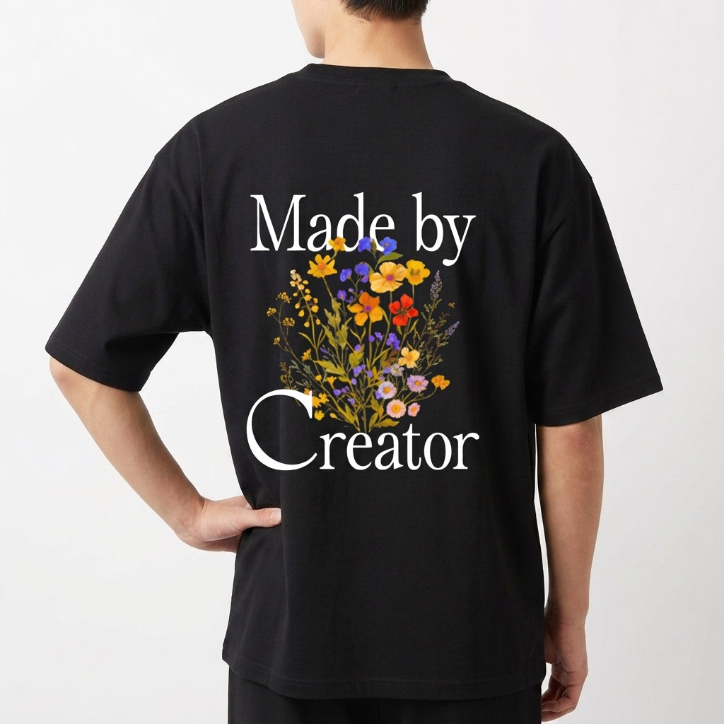 Camiseta com estampa frontal de texto estilizado "Made by Creator" e estampa traseira de flores vibrantes entre o texto "Made by Creator".