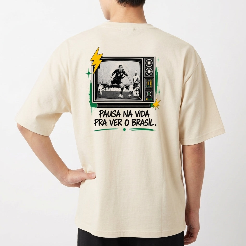 Camiseta com estampa frontal de "Modo Brasil On" ao lado de um raio estilizado e estampa traseira de TV retrô com jogador de futebol e frase inspiradora.