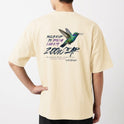 Camiseta com estampa frontal de beija-flor em voo circular e estampa traseira de beija-flor em destaque cercado por texto artístico estilizado.