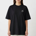 Camiseta com estampa frontal de pequeno símbolo circular com seta apontando para cima no lado esquerdo do peito e estampa traseira de surfista em túnel de onda dinâmica com efeitos de pinceladas.