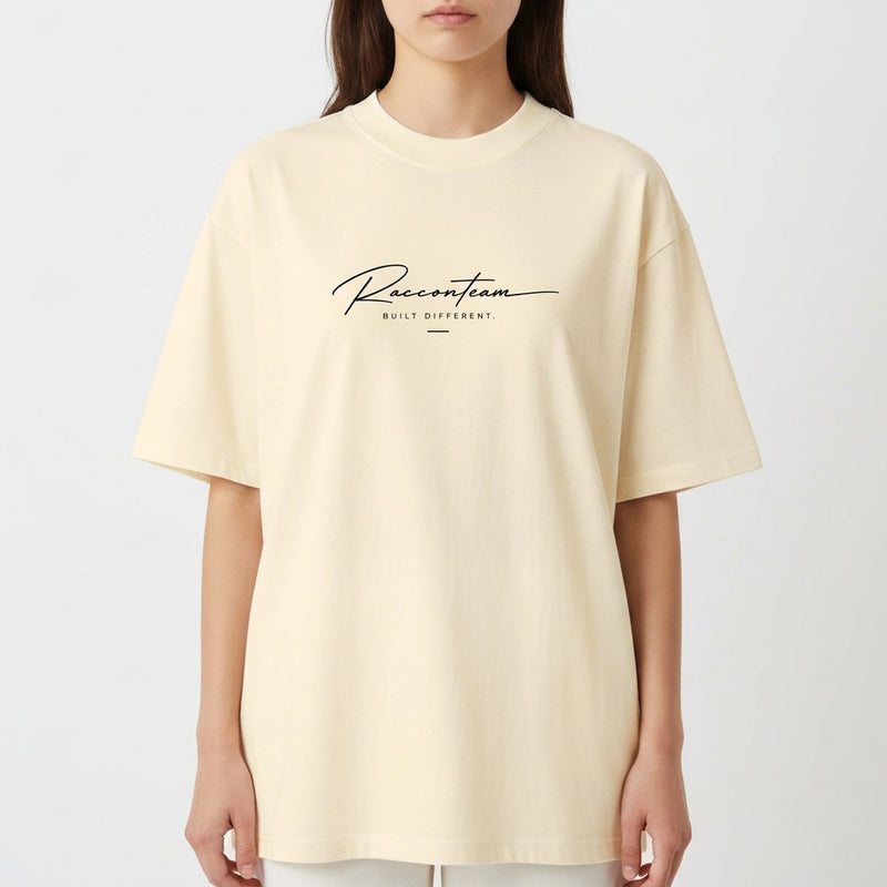 Camiseta com estampa frontal de lettering cursivo "Racoon Team - Built Different" e estampa traseira de iniciais grandes "RT", texto "Raccon Team - Est. 2017".