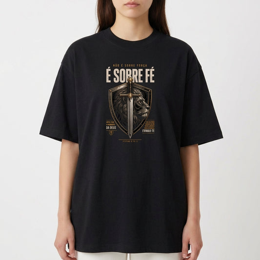 Camiseta com estampa frontal de escudo contendo uma espada centralizada e a imagem de um leão ao fundo, com textos ao redor enfatizando fé.