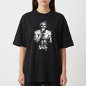 Camiseta com estampa frontal de uma figura masculina segurando um microfone, envolta de efeitos gráficos, com o nome "Nelly" em letras cursivas abaixo.