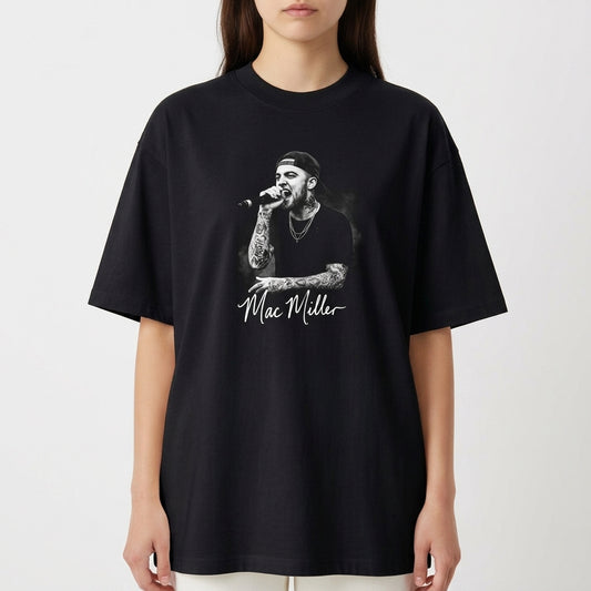 Camiseta com estampa frontal de um artista cantando no microfone, vestindo boné e camisa preta, destacando tatuagens nos braços e autógrafo abaixo.