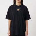 Camiseta com estampa frontal de cabeça de animal estilizada com dois olhos e estampa traseira de personagem em design geométrico acompanhada de textos e detalhes.