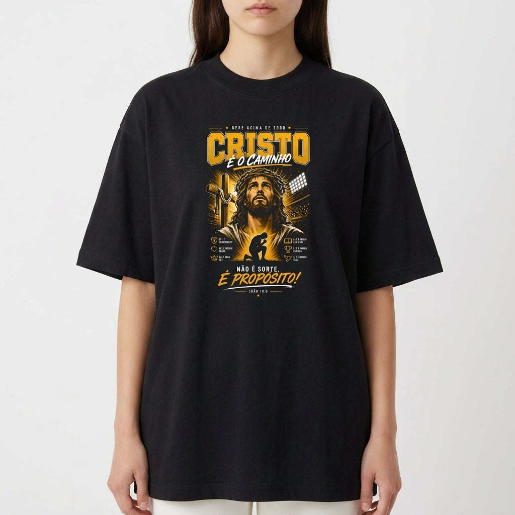 Camiseta com estampa frontal de uma figura religiosa cercada por textos e elementos gráficos detalhados, incluindo frases em destaque e simbologia variada.