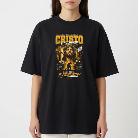 Camiseta com estampa frontal de uma figura religiosa cercada por textos e elementos gráficos detalhados, incluindo frases em destaque e simbologia variada.