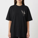 Camiseta com estampa frontal de figura angelical detalhada com asas abertas e envolta em detalhes intricados, compondo um design de estética celestial.