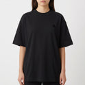 Camiseta com estampa frontal de pequeno logotipo estilizado e estampa traseira de personagem em quadrinhos com frase em destaque e elementos gráficos.