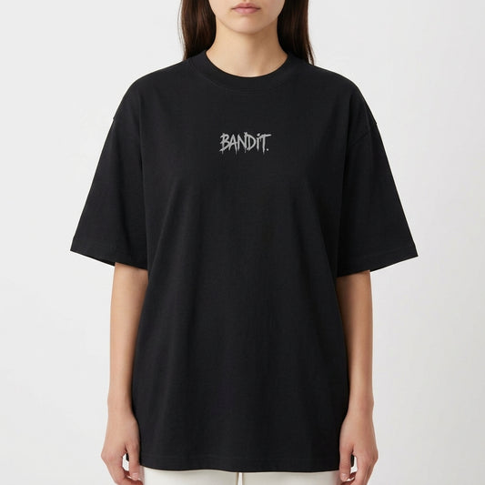 Camiseta com estampa frontal de texto estilizado "Bandit" e estampa traseira de frase "Chaos is Currency", ambos com letras em estilo desgastado.